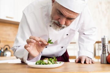 male cook chef decorating garnishing prepared salad dish on the plate in restaurant commercial kitchen.