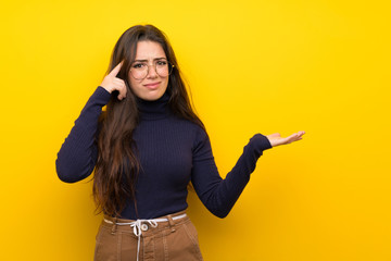 Teenager girl over isolated yellow wall making the gesture of madness putting finger on the head