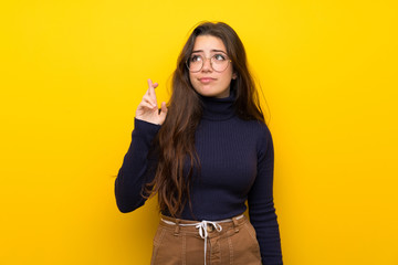 Teenager girl over isolated yellow wall with fingers crossing and wishing the best