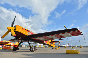 Beautiful yellow piston aircraft with a propeller is parked at the airport against a blue sky with clouds. Close-up