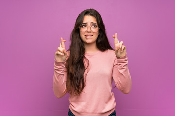 Teenager girl over purple wall with fingers crossing and wishing the best