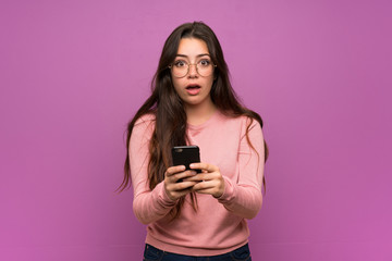Teenager girl over purple wall surprised and sending a message