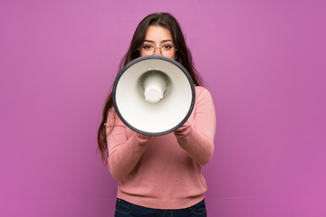 Teenager girl over purple wall shouting through a megaphone