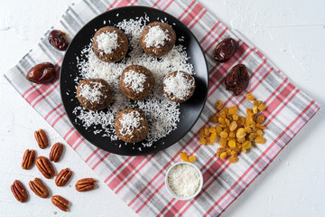 Healthy organic energy balls made with dates, prunes, raisins, peanut, with coconut shavings, in black plate on white background.