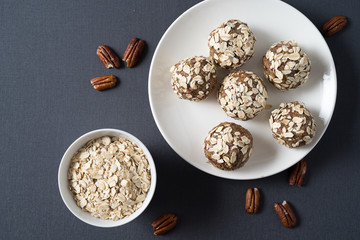 Healthy organic energy balls made with dates, oat flakes, dried cranberries, pecan nuts, in a plate on gray background.