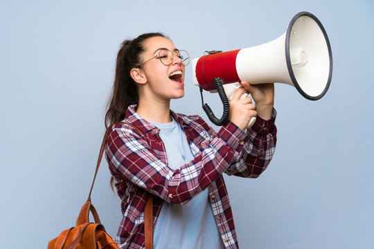 Teenager Student Girl Over Isolated Blue Wall Shouting Through A Megaphone