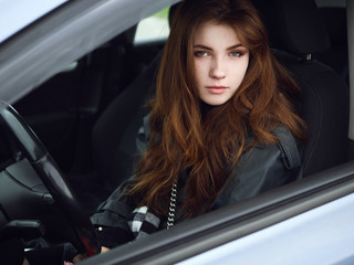 Fototapeta na wymiar Close up portrait of young attractive red hair self-employed business woman driver sitting in white car stuck in a city traffic jam staring into camera running late to work noonday bleached colors