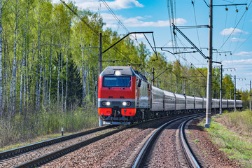 Passenger train approaches to the station at spring day time.