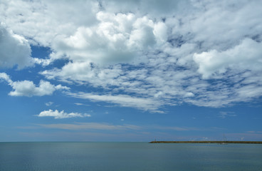 Fototapeta na wymiar Hintergrund mit Meer und blauem Himmel mit Wolken vor einer zarten Küstenlinie