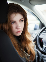 Fototapeta na wymiar Close up portrait of young attractive red hair self-employed business woman driver looking back from the driver's seat stuck in a city traffic jam noonday bleached colors cloudy weather