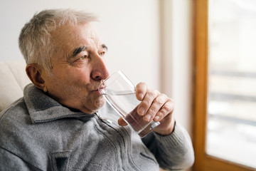 Senior man old sitting drinking glass of water by the window at the retirement nursing home
