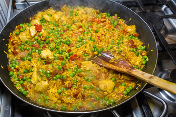 Cooking chicken paella with wooden spatula and green peas