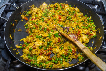 Cooked chicken paella with wooden spatula and green peas on hob