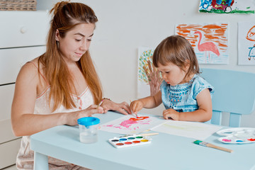 woman with a little girl holding a drawing lesson in the room at the table.