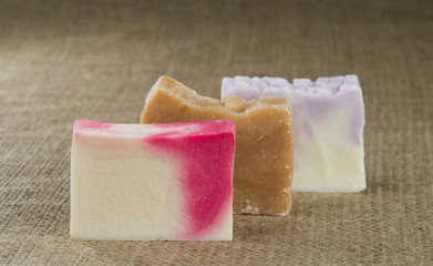 Three different handmade pieces of soap on a background of rough burlap texture.