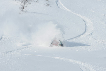 Fototapeta na wymiar A snowboarder falling into deep snow at the ski resort in a sunny morning