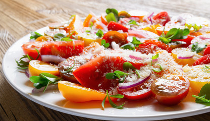pear, rose, cherry, black, and plum tomato variety salad with leaf vegetables in european white plate on wooden top