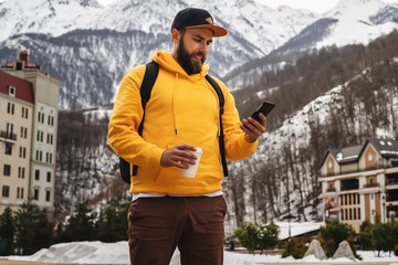Front view. Man tourist in yellow hoodie, cap with backpack stands on background of high snowy...