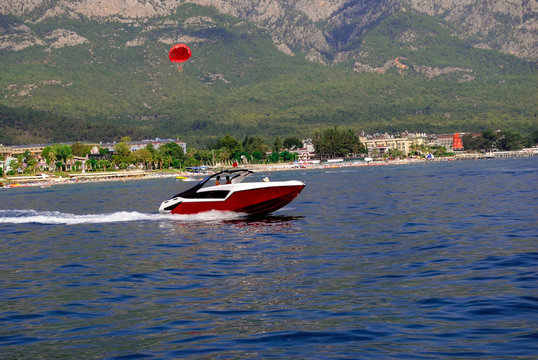 Red speedboat with red parashute on a sea and mountain background