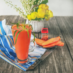 Fresh homemade vegetable juice from carrots and tarragon in a glass Cup. With carrots and yellow flowers