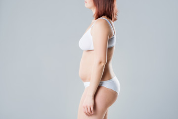 Woman with fat flabby belly, overweight female body on gray background