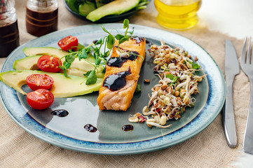 A piece of baked red fish with a side dish of sprouts and avocado salad. Macrobiotic food concept. Healthy food