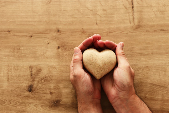 Adult male hands holding wooden shaped heart over table