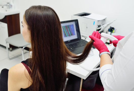 doctor dermatologist diagnoses the structure of the hair of a young pretty girl with a special tool - a trichoscope. Trichology, trichogram