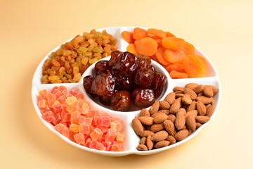 Mix of dried fruits and nuts on a white plate. Apricot, almond, raisin, dates fruit. On a beige background. Space for text or design.