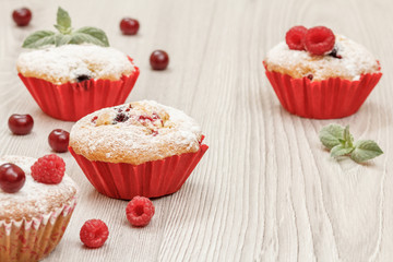 Homemade cupcakes sprinkled with powdered sugar and fresh raspberries and mint.