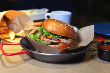 Delicious tasty burger with beef, tomatoes, salad and sauce on wooden table and black background.  Space for text or design.