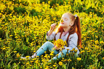 portrait of a child - a little cute red-haired girl on the background of a field of dandelions and greenery.