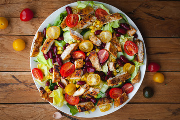 Close-up of chicken salad with fresh vegetables in a plate, on wooden background, top view