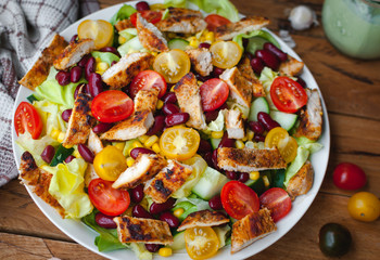 Close-up of chicken salad with fresh vegetables in a plate, on wooden background
