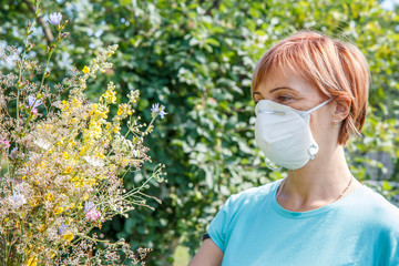 Woman in protection mask holding bouquet of wildflowers and trying to fight allergies