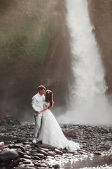 Fototapeta na wymiar Young couple in love bride and groom, wedding day near a mountain waterfall. Enjoy a moment of happiness and love. Bride in a luxurious wedding dress