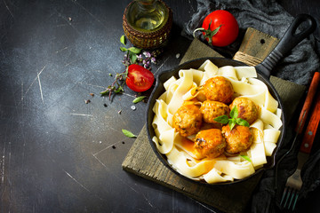 Fettuccine pasta and Homemade Beef meatballs in tomato sauce in a frying pan on dark stone table. Free space for your text.