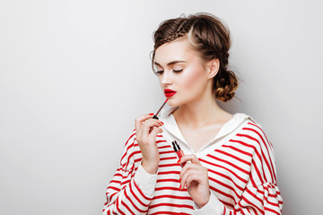 Young woman with red lips on pretty emotional face in elegant dress holding makeup lipstick in studio isolated on white background