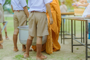 Teachers and students together make merit to give food offerings to a Buddhist monk on important religious days at school.