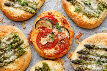 Small pizzas with the addition of green asparagus, tomatoes, cheese and herbs, top view, close-up. Vegetarian pizzas, delicious appetizer