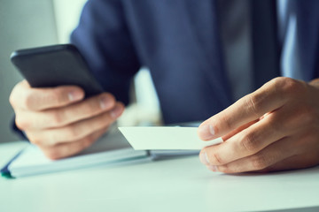 Businessman holding blank business card and dialing numbers on mobile phone