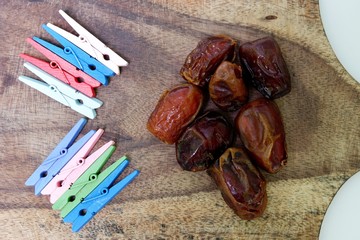 Closeup sweet dried date palm fruits/kurma, ramdhan food and Colourful clothespins collection the wooden base of a tray (tatakan kayu) isolated on white background. Top up view close up details.
