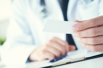 Male physician hand holding and giving white blank calling card closeup in office. Contact information exchange, introducing gesture at formal meeting, personal or family doctor concept