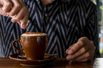 Man hands pouring sugar to the cappuccino or latte cup in cafe