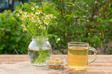 Glass cup of green tea with white chamomile flowers in a glass jar outdoor.