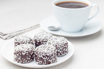 Swedish sweets chocolate balls or chokladbollar, made from oats, cocoa, butter and coconut, on white plate, served with coffee,  horizontal