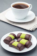 Swedish sweets punsch rolls or punschrullar, covered with green marzipan, on white plate, served with coffee,  vertical
