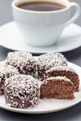 Swedish sweets chocolate balls or chokladbollar, made from oats, cocoa, butter and coconut, on white plate, served with coffee,  vertical