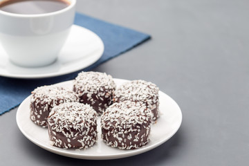 Swedish sweets chocolate balls or chokladbollar, made from oats, cocoa, butter and coconut, on white plate, served with coffee,  horizontal, copy space