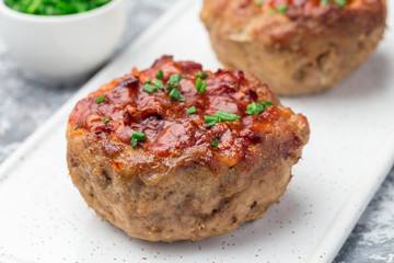 Low carb paleo meat cups, stuffed with champignons, bacon and cheese, garnished with green onion, on white plate, horizontal, closeup